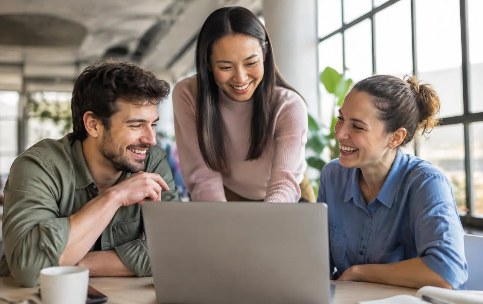Three colleagues laughing together around a laptop