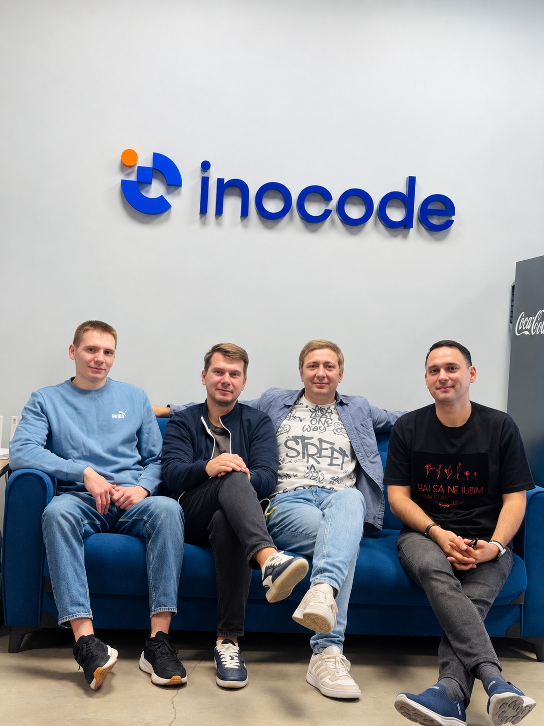 Four Inocode team members sitting together in front of the Inocode office logo wall